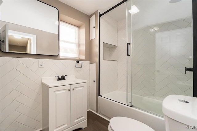 full bathroom with vanity, toilet, bath / shower combo with glass door, and tile walls