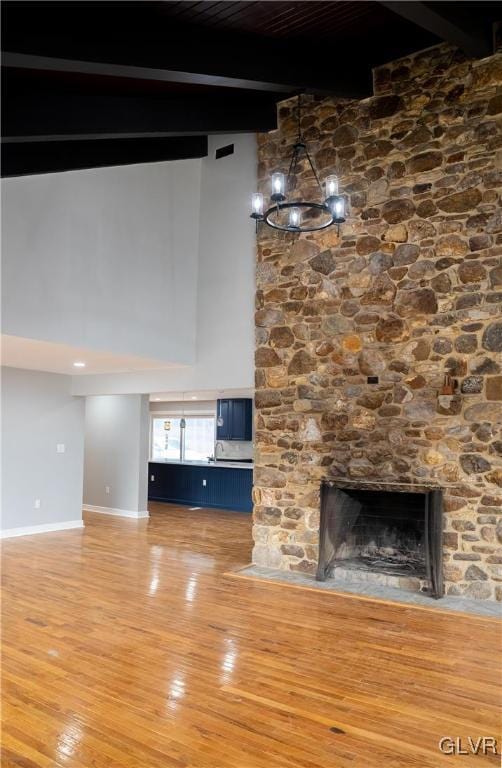 unfurnished living room with a stone fireplace, an inviting chandelier, beamed ceiling, and hardwood / wood-style flooring