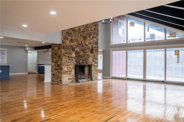 unfurnished living room with wood-type flooring, a stone fireplace, and a notable chandelier