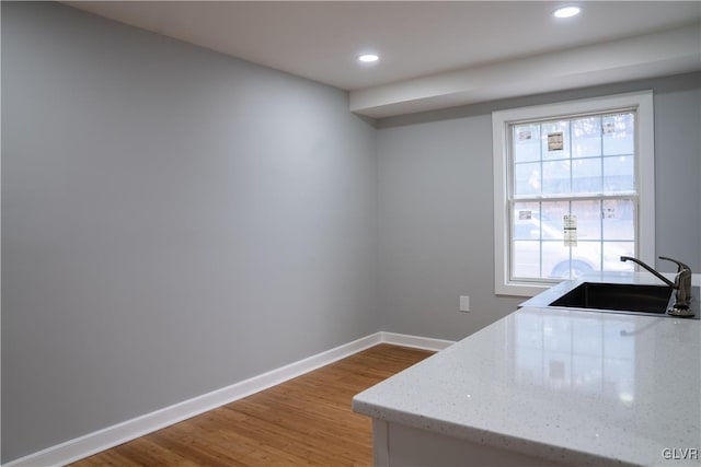 kitchen with light stone countertops, wood-type flooring, and sink