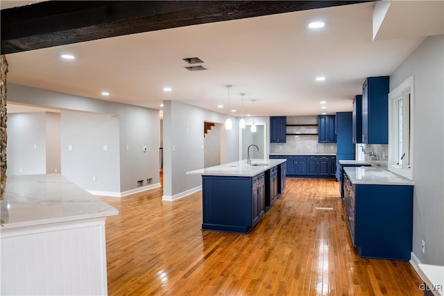 kitchen with a center island with sink, light hardwood / wood-style flooring, decorative light fixtures, and blue cabinets