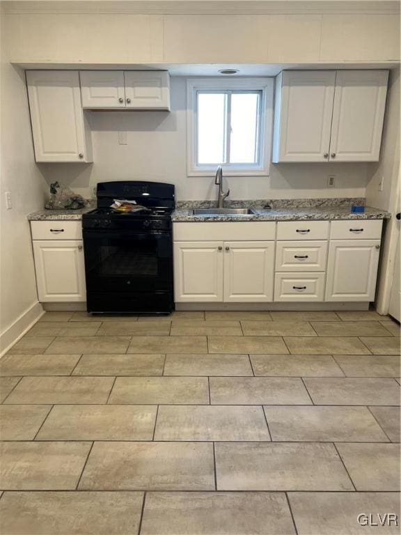 kitchen with light stone countertops, black gas range oven, white cabinetry, and sink