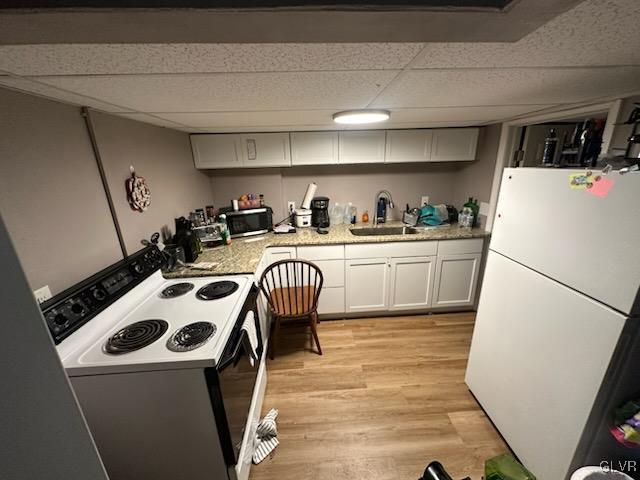 kitchen with a paneled ceiling, white appliances, white cabinets, sink, and light hardwood / wood-style floors