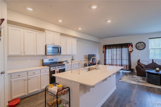 kitchen with appliances with stainless steel finishes, dark hardwood / wood-style flooring, sink, a center island with sink, and white cabinets