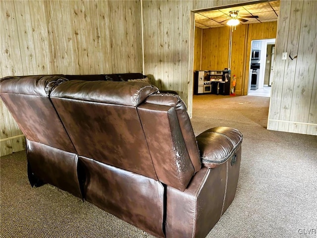 carpeted living room with ceiling fan and wooden walls