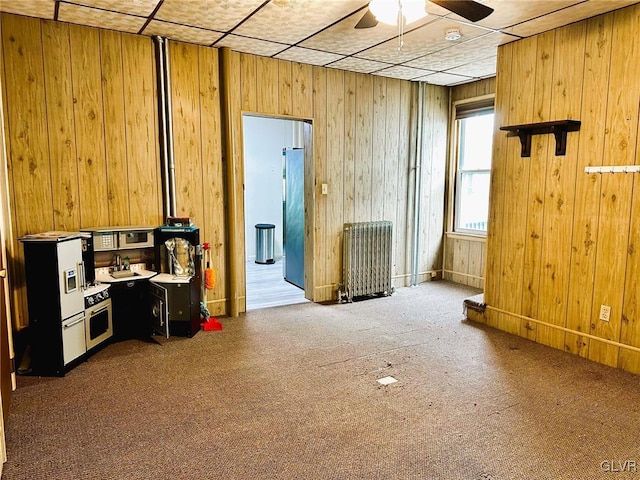 interior space featuring carpet floors, ceiling fan, wooden walls, and radiator heating unit