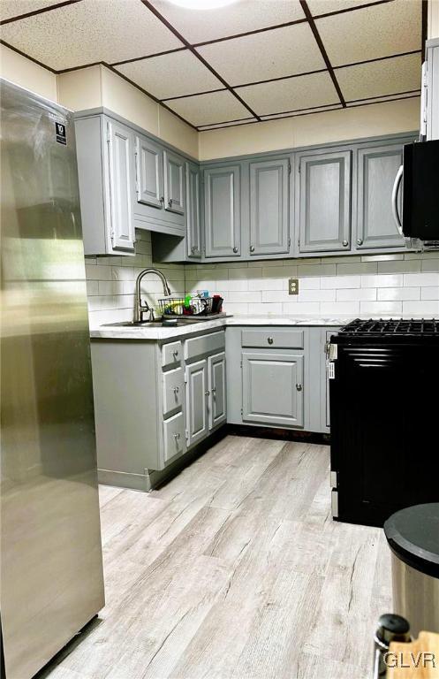 kitchen with stainless steel appliances, decorative backsplash, gray cabinets, a drop ceiling, and light hardwood / wood-style flooring