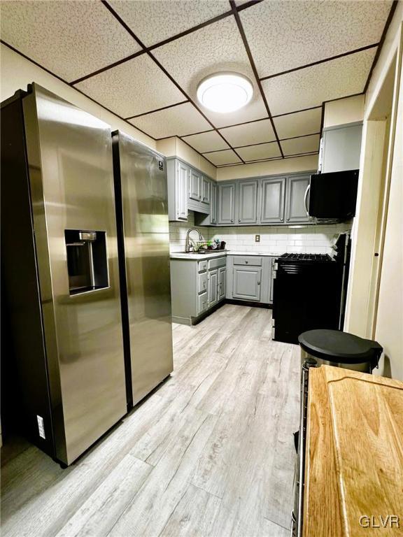 kitchen with stainless steel fridge with ice dispenser, gray cabinets, a drop ceiling, range, and light hardwood / wood-style flooring