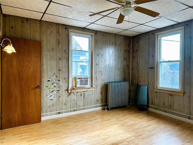 empty room with ceiling fan, light hardwood / wood-style floors, wooden walls, cooling unit, and radiator heating unit