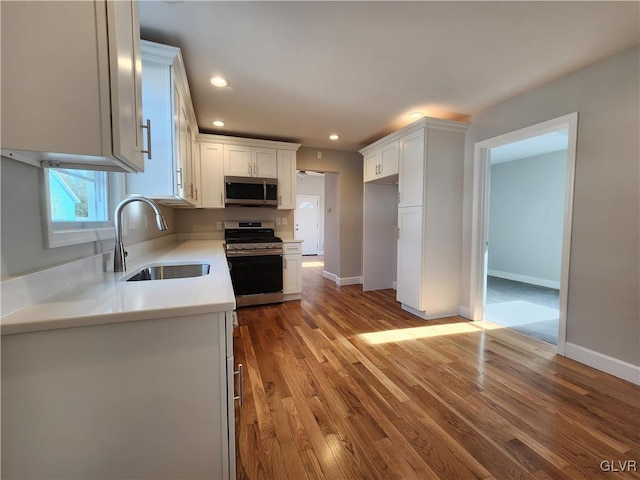 kitchen with white cabinets, appliances with stainless steel finishes, hardwood / wood-style flooring, and sink