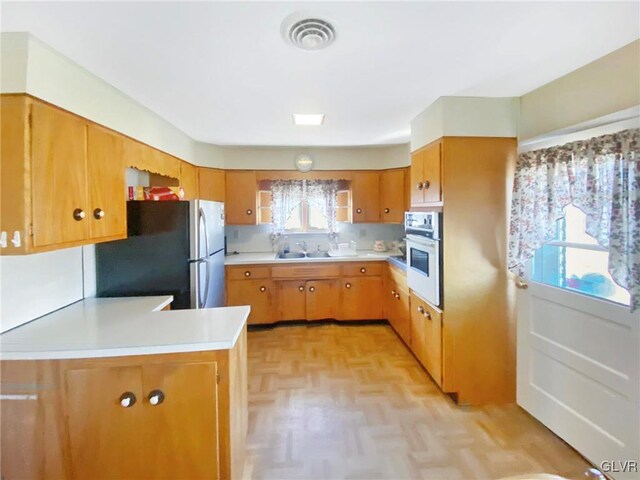 kitchen featuring kitchen peninsula, wall oven, stainless steel refrigerator, and a wealth of natural light