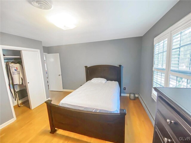 bedroom with a closet, light hardwood / wood-style flooring, and a baseboard heating unit