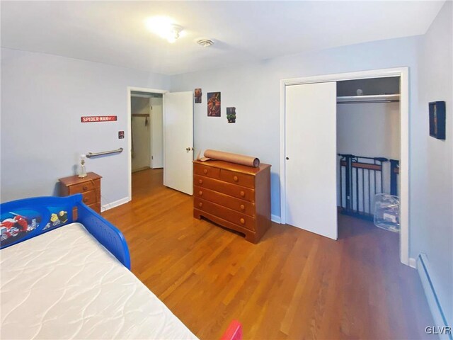 bedroom with a closet, hardwood / wood-style floors, and a baseboard heating unit