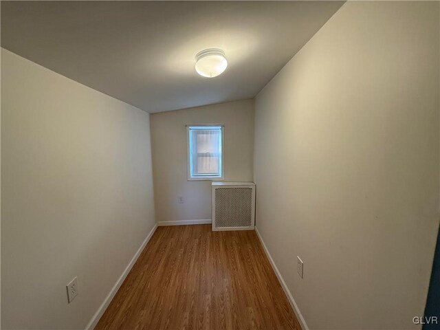 spare room with vaulted ceiling, radiator heating unit, and light hardwood / wood-style flooring