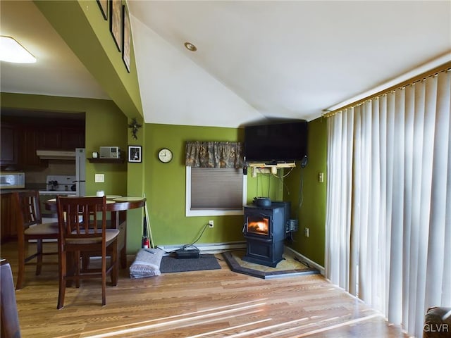 kitchen with white appliances, light wood-type flooring, high vaulted ceiling, and a wood stove