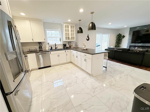 kitchen featuring kitchen peninsula, stainless steel appliances, sink, decorative light fixtures, and white cabinetry