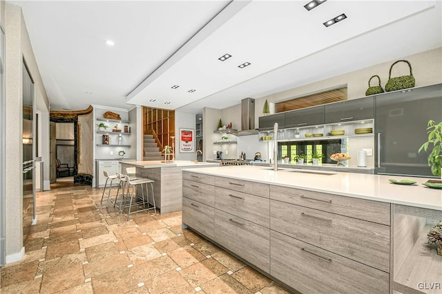 kitchen with wall chimney exhaust hood, a breakfast bar, and a center island