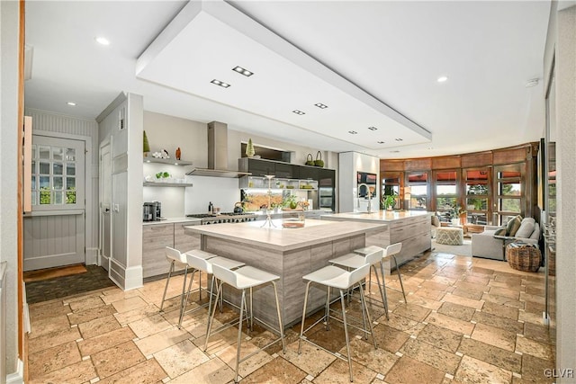 kitchen with a breakfast bar area, wall chimney exhaust hood, a spacious island, and stainless steel gas stovetop