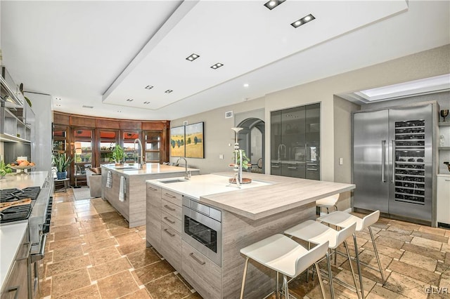 kitchen featuring a breakfast bar area, built in appliances, a center island with sink, and sink