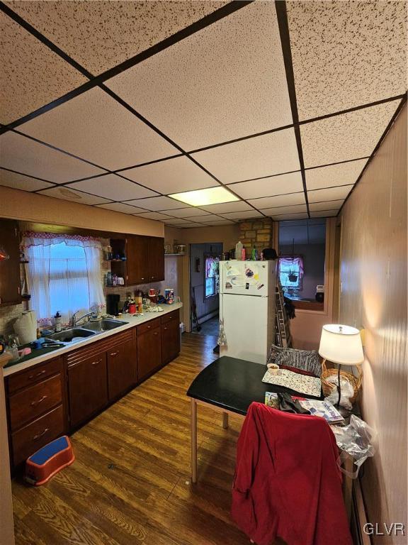 kitchen featuring dark brown cabinetry, sink, a drop ceiling, white refrigerator, and hardwood / wood-style floors