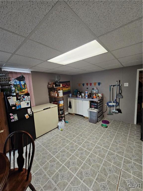 basement featuring a paneled ceiling and fridge