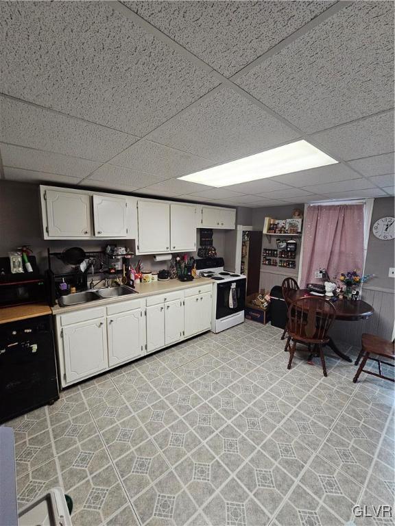 kitchen with a paneled ceiling, white range with electric stovetop, white cabinetry, and sink