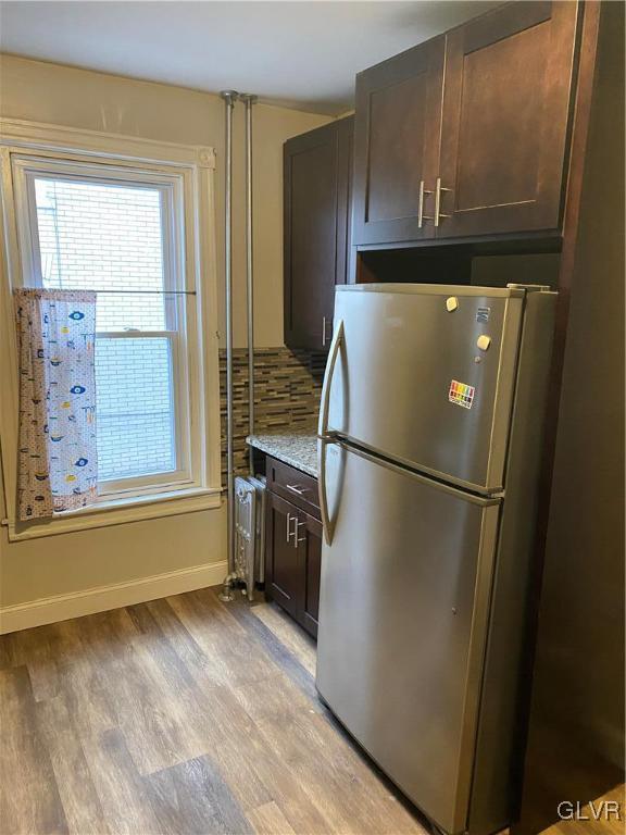 kitchen featuring stainless steel refrigerator, light stone countertops, dark brown cabinets, and light hardwood / wood-style floors