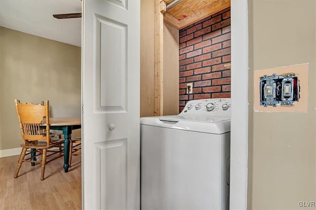 washroom with light wood-type flooring, washer / clothes dryer, and brick wall