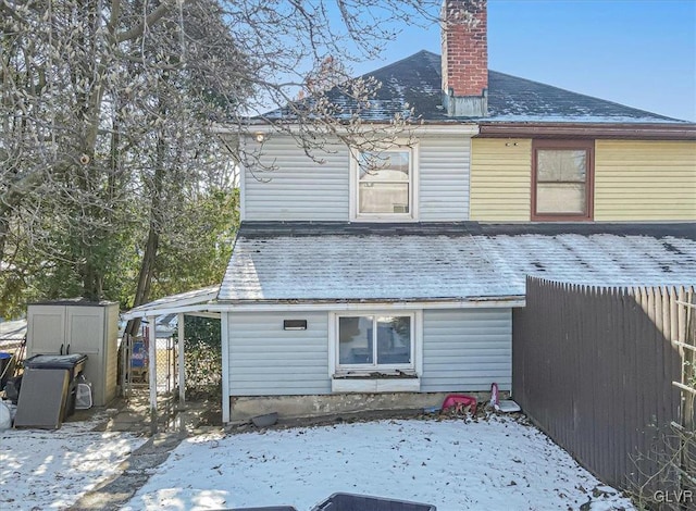 snow covered rear of property featuring a storage unit