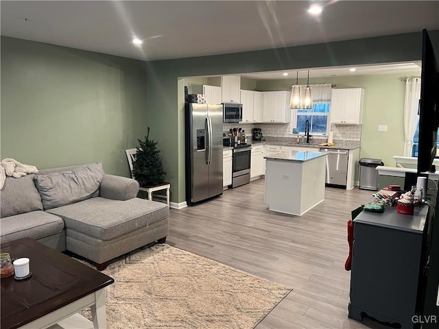 kitchen with white cabinetry, a center island, light hardwood / wood-style flooring, decorative light fixtures, and appliances with stainless steel finishes