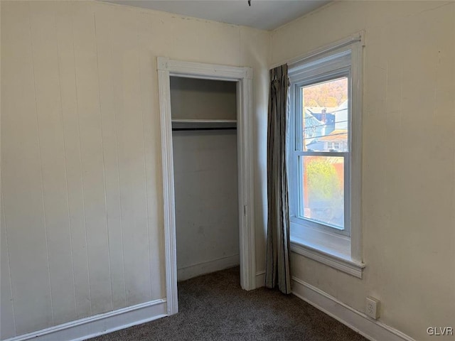 unfurnished bedroom with dark carpet, wooden walls, and a closet