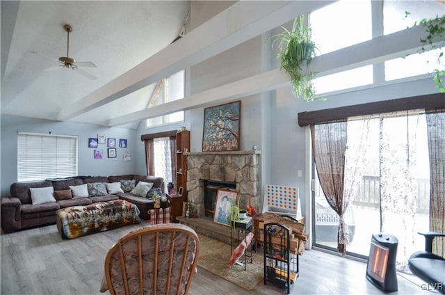 living room with ceiling fan, a towering ceiling, a fireplace, and light hardwood / wood-style flooring