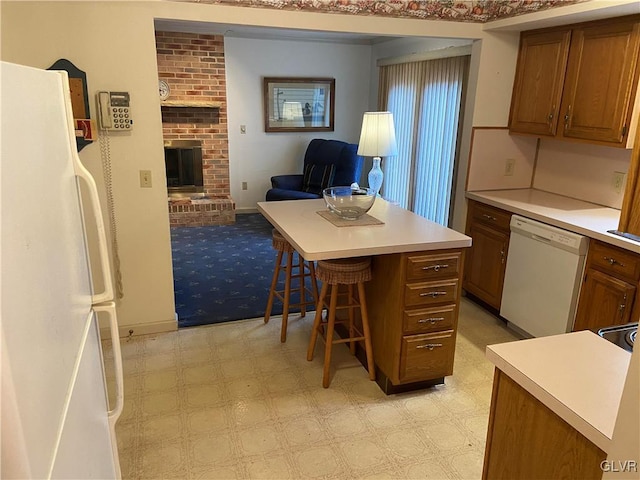 kitchen featuring a kitchen breakfast bar, white appliances, a kitchen island, and a brick fireplace