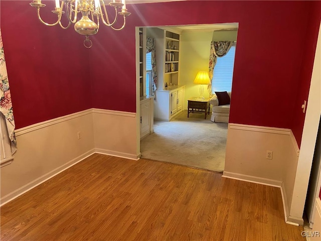 spare room featuring built in shelves, a chandelier, and light wood-type flooring