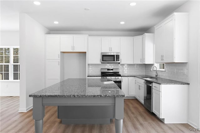 kitchen featuring dark stone counters, stainless steel appliances, sink, light hardwood / wood-style flooring, and a center island