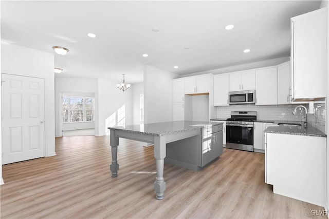 kitchen featuring light wood-type flooring, stainless steel appliances, a kitchen island, dark stone countertops, and white cabinetry