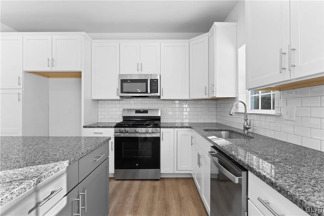 kitchen with appliances with stainless steel finishes, sink, dark stone countertops, white cabinets, and hardwood / wood-style floors