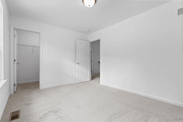 unfurnished bedroom with a spacious closet, a closet, and light colored carpet