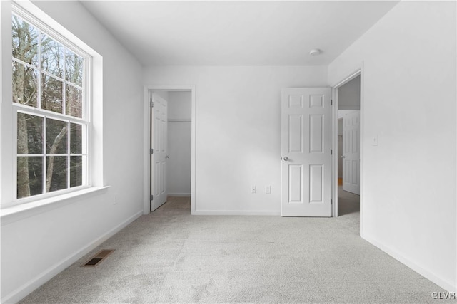 unfurnished bedroom featuring a spacious closet, a closet, and light colored carpet