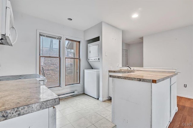 kitchen featuring stacked washing maching and dryer, sink, a baseboard radiator, light hardwood / wood-style flooring, and white cabinetry