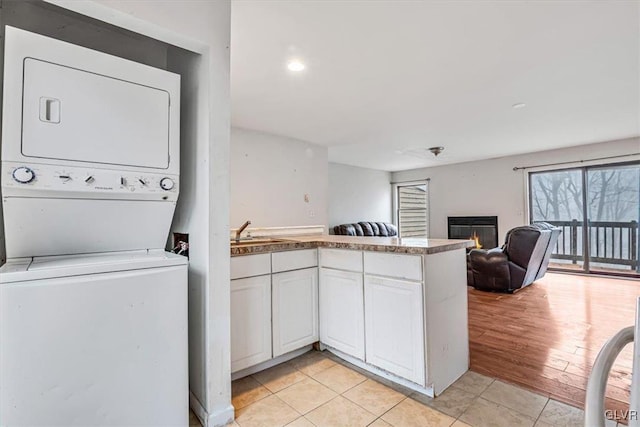 kitchen with kitchen peninsula, light wood-type flooring, sink, stacked washer and clothes dryer, and white cabinets