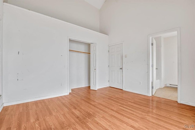 unfurnished bedroom featuring light hardwood / wood-style floors, high vaulted ceiling, baseboard heating, and ensuite bathroom