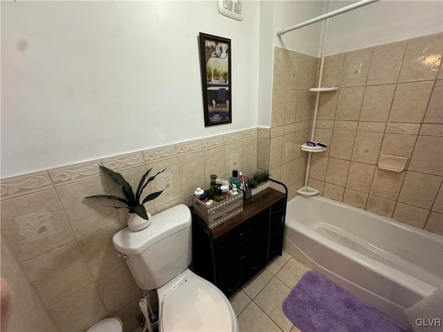 bathroom with tile patterned flooring, tiled shower / bath, toilet, and tile walls