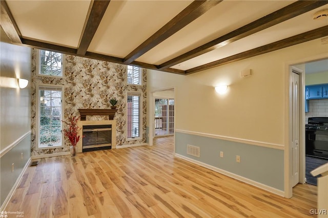 unfurnished living room featuring beam ceiling, light wood-type flooring, and a high end fireplace