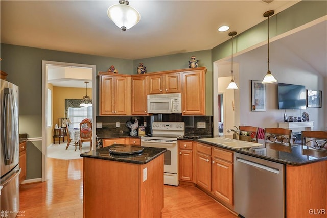 kitchen with a center island, sink, light wood-type flooring, appliances with stainless steel finishes, and decorative light fixtures