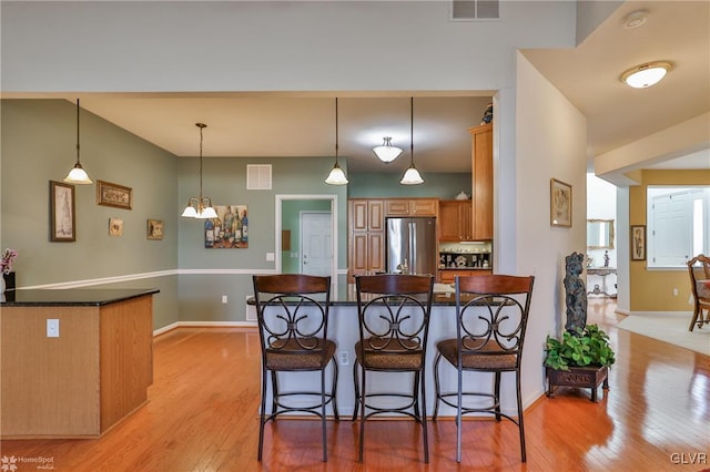 kitchen featuring stainless steel refrigerator, kitchen peninsula, a breakfast bar, and light wood-type flooring