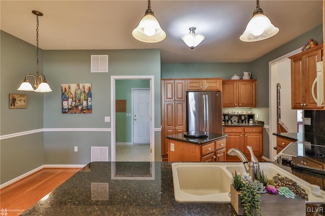 kitchen with pendant lighting, a center island, an inviting chandelier, stainless steel fridge, and light wood-type flooring