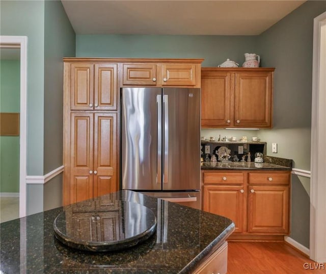 kitchen with light wood-type flooring, stainless steel refrigerator, and dark stone counters