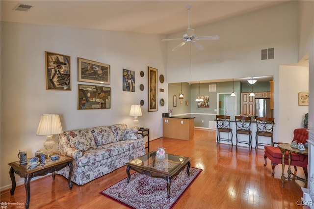 living room featuring high vaulted ceiling, light hardwood / wood-style floors, and ceiling fan with notable chandelier