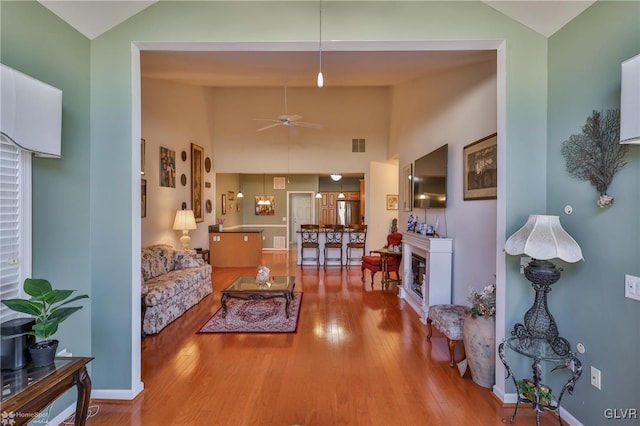 living room with ceiling fan, wood-type flooring, and a high ceiling